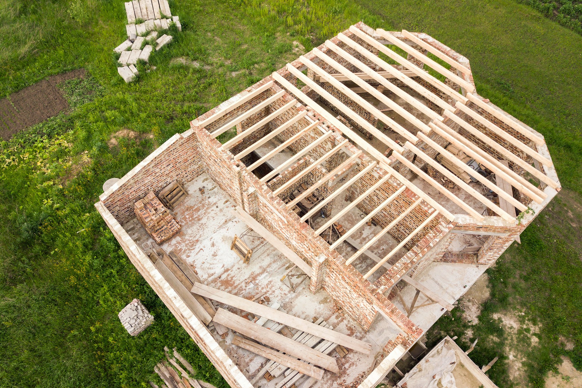 Aerial view of a brick house with wooden ceiling frame under construction.