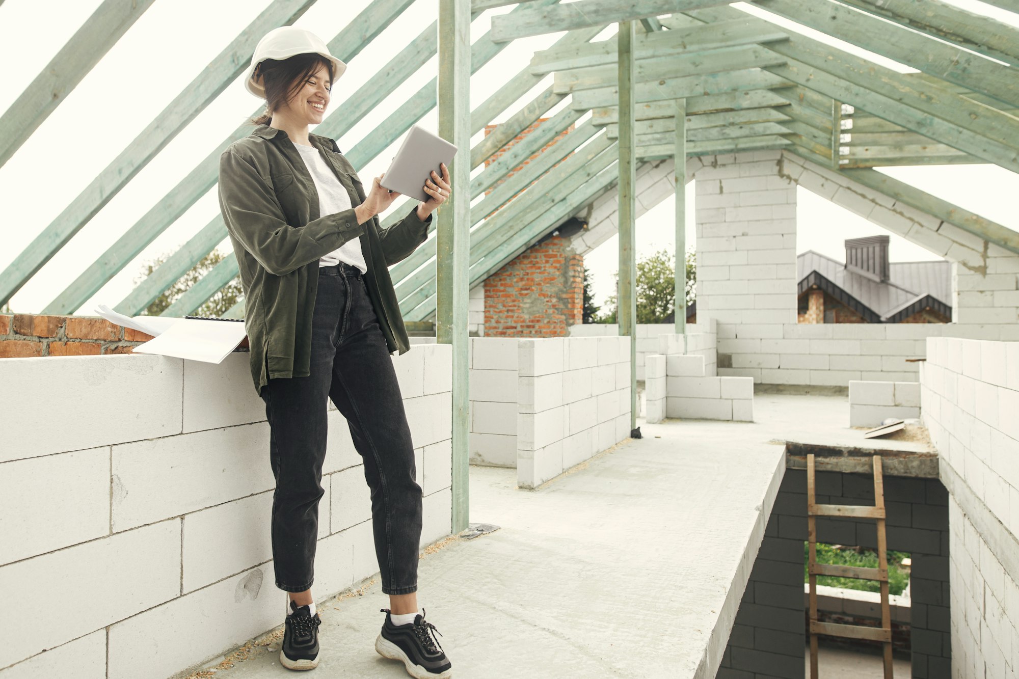 Stylish woman architect or engineer with tablet checking blueprints at wooden roof framing